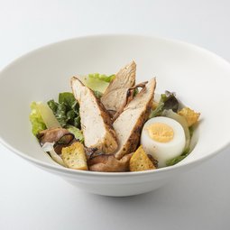 Caesar salad with herb croutons, grilled chicken pieces, roasted bacon and egg